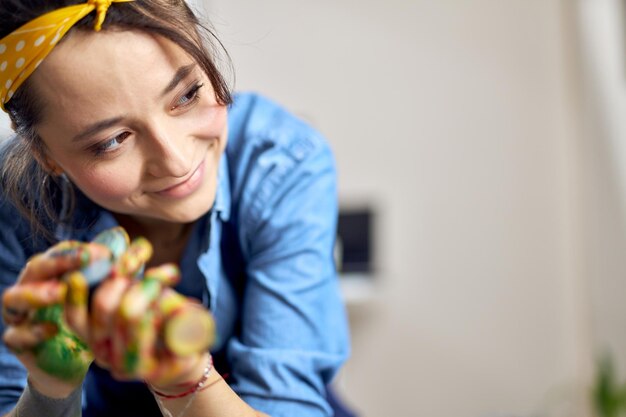 Retrato de mujer joven complacida con las manos en pintura colorida de cerca sonriendo a un lado