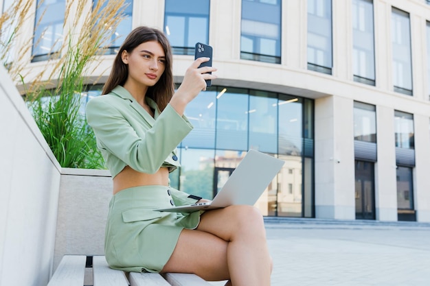 Retrato de una mujer joven con una computadora portátil afuera Mujer de negocios mientras trabaja en la calle sentada en un banco