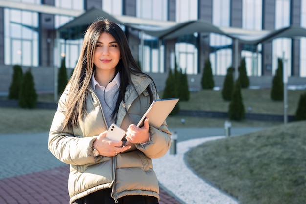 Retrato de una mujer joven con computadoras portátiles en el fondo de un edificio de oficinas