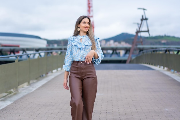 Retrato de mujer joven en un concepto de estilo de vida del puente del río de la ciudad camisa azul y pantalones marrones