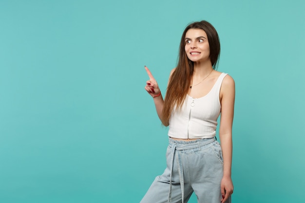 Retrato de mujer joven confundida en ropa casual ligera mirando hacia un lado con el dedo índice aislado sobre fondo de pared azul turquesa. Personas sinceras emociones, concepto de estilo de vida. Simulacros de espacio de copia.