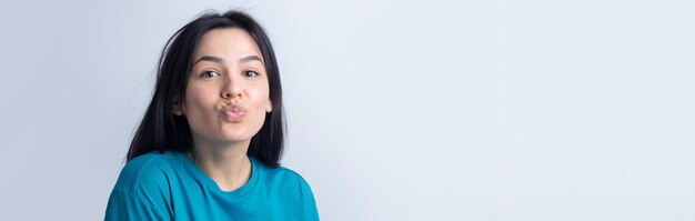 Retrato de mujer joven coqueteando soplando aire beso aislado sobre fondo gris