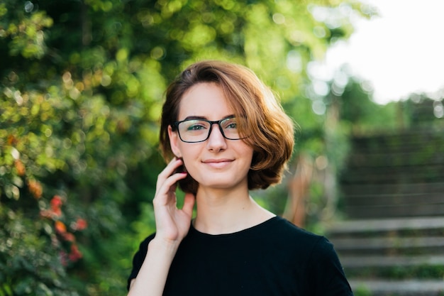 Retrato de una mujer joven con un corte de pelo corto y gafas al aire libre