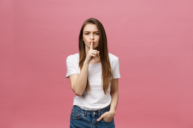 Retrato de mujer joven con el dedo en los labios contra la pared rosa