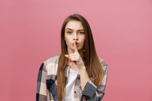 Retrato de mujer joven con el dedo en los labios contra la pared rosa