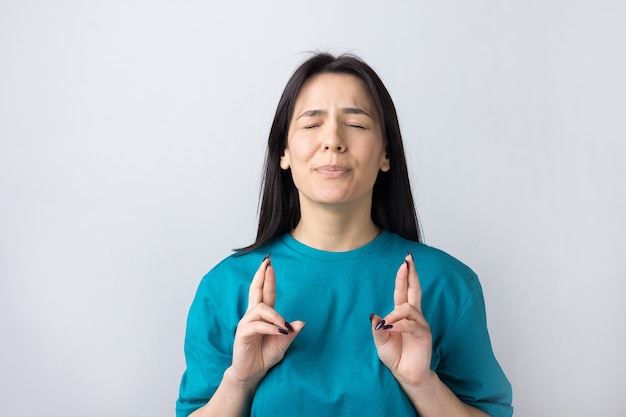 Retrato de mujer joven deseosa que cruza los dedos y espera suerte.