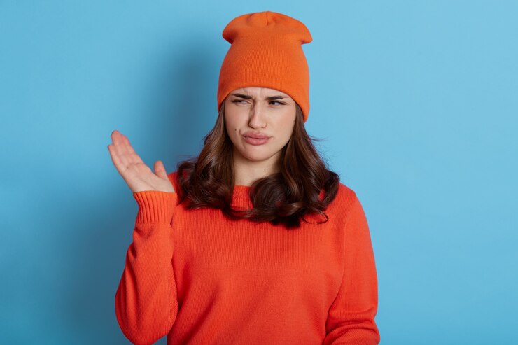 Foto retrato de mujer joven disgustada siente olor apestoso, tiene expresión de descontento, se viste de jersey y suéter casual, posa en azul