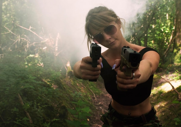 Foto retrato de una mujer joven disparando con una pistola en el bosque