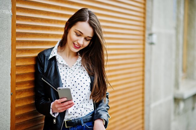 Retrato de mujer joven elegante vistiendo chaqueta de cuero con teléfono móvil a mano