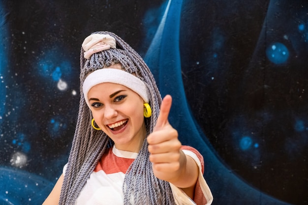 Foto retrato de mujer joven emocionada con rastas o coletas kanekalon mirando a cámara y sonriendo