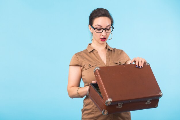 Retrato de mujer joven emocionada sosteniendo una maleta aislada sobre pared azul, viajes, vacaciones