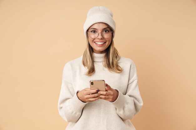 Retrato de mujer joven encantada en anteojos sonriendo y escribiendo en el teléfono inteligente
