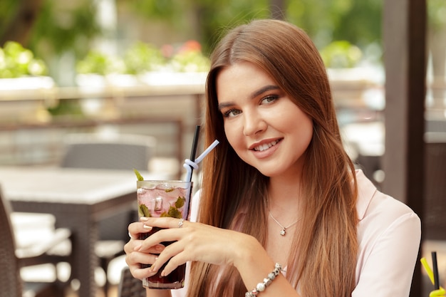 Retrato de mujer joven encantadora que sostiene un vaso de cóctel refrescante frío