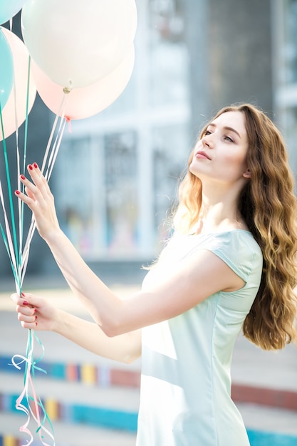 Retrato de mujer joven de ensueño con globos multicolores voladores en la ciudad