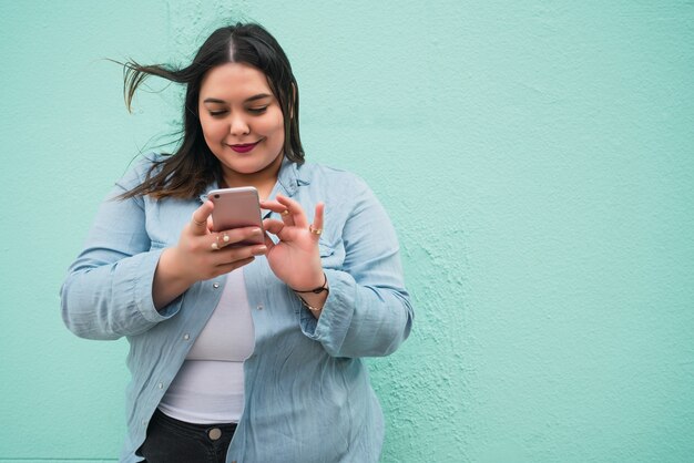 Retrato de mujer joven escribiendo un mensaje de texto en su teléfono móvil al aire libre