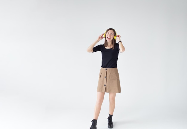 Retrato de una mujer joven escuchando música con auriculares amarillos sobre un fondo blanco aislado