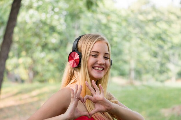 Retrato de mujer joven escuchando música con auriculares y sonriendo en el parque.