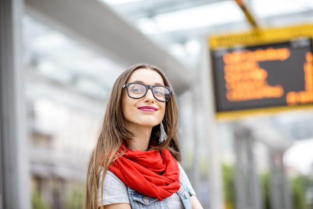 Retrato de una mujer joven esperando el transporte público de pie en la parada del tranvía con el horario en el fondo