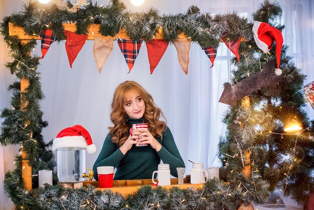 Retrato de mujer joven está bebiendo té cerca del coche rojo, decorado con árboles de Navidad y guirnaldas