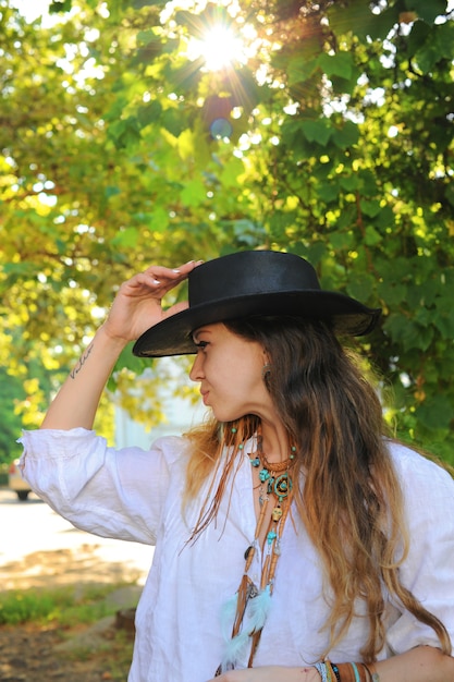 Retrato de mujer joven estilo hipster en el parque de la ciudad, día soleado, sombrero negro de cuero