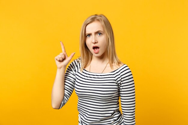 Retrato de una mujer joven estricta con ropa a rayas jurando, señalando con el dedo índice aislado en el fondo de la pared naranja amarilla en el estudio. Gente emociones sinceras concepto de estilo de vida. Simulacros de espacio de copia.