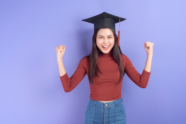 Retrato de mujer joven estudiante universitaria con gorro de graduación sobre fondo violeta