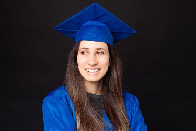 Retrato de mujer joven estudiante vistiendo túnica azul y gorro de graduación