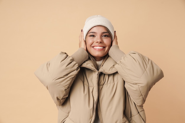 Retrato de mujer joven feliz en abrigo de invierno agarrando su cabeza y sonriendo