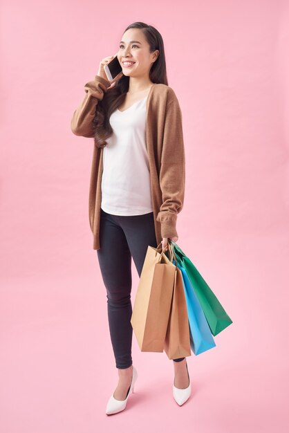 Retrato de mujer joven feliz con bolsas de la compra hablando por teléfono móvil