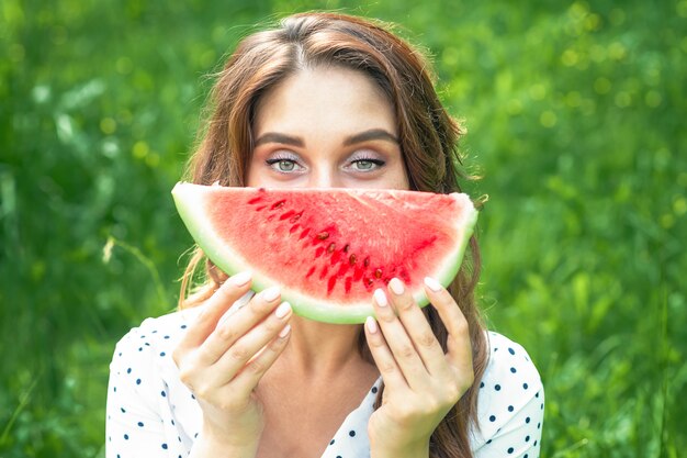 El retrato de la mujer joven feliz está sosteniendo la rebanada de sandía sobre fondo verde.