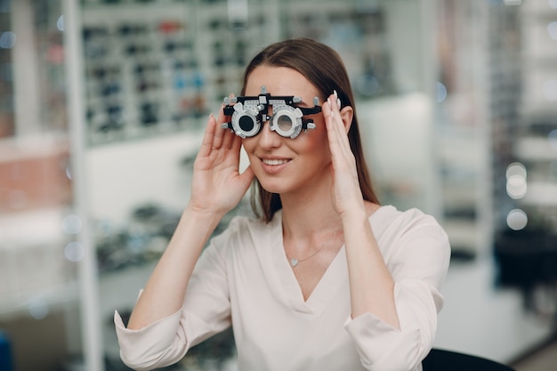 Retrato de mujer joven feliz durante el examen de la vista con gafas de prueba en el óptico optometrista