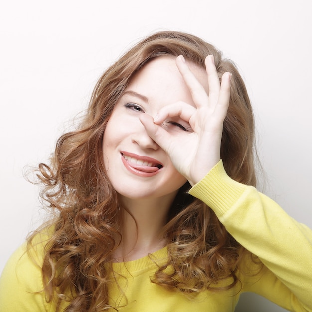 Retrato de una mujer joven feliz haciendo signo bien contra la pared blanca