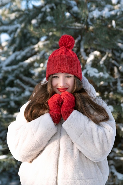 Retrato de mujer joven feliz con labios rojos en sombrero rojo de punto y mitones en bosque nevado Caperucita roja