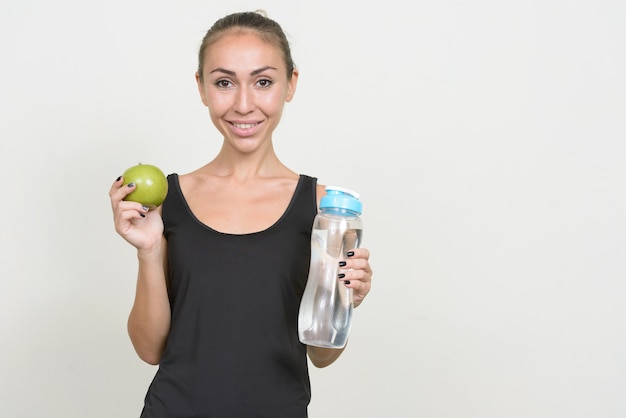 Retrato de mujer joven feliz con manzana y botella de agua listo para gimnasio