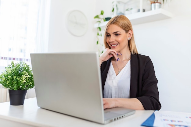 Retrato de mujer joven feliz mirando portátil trabajando en casa. Señora exitosa riendo y trabajando en casa. Hermosa mujer elegante sonriendo y trabajando en casa.