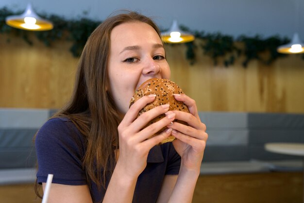 Foto retrato de una mujer joven feliz o una hermosa adolescente comiendo comida chatarra rápida, una hamburguesa sabrosa y