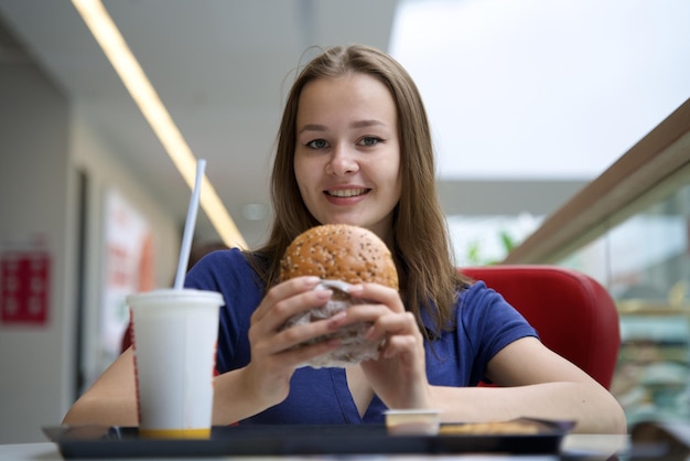 Foto retrato de una mujer joven feliz o una hermosa adolescente comiendo comida chatarra rápida, una hamburguesa sabrosa y