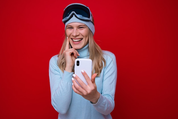 Retrato de una mujer joven feliz en un suéter y gafas de esquí con un teléfono