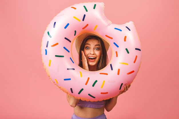 Retrato de una mujer joven feliz vestida en traje de baño saltando y sosteniendo nadar anillo inflable