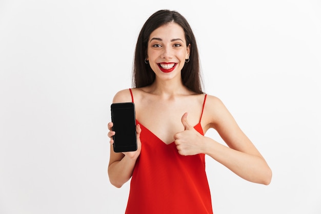 Retrato de una mujer joven feliz en vestido aislado, mostrando teléfono móvil de pantalla en blanco