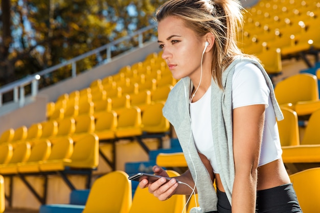 Retrato de una mujer joven fitness sosteniendo el smartphone en el estadio al aire libre