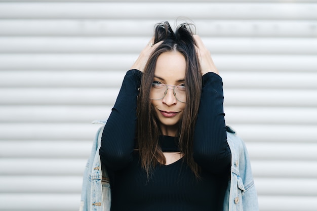 Retrato de mujer joven con gafas. Mujer de estilo bonito con cabello largo oscuro con una chaqueta de mezclilla.