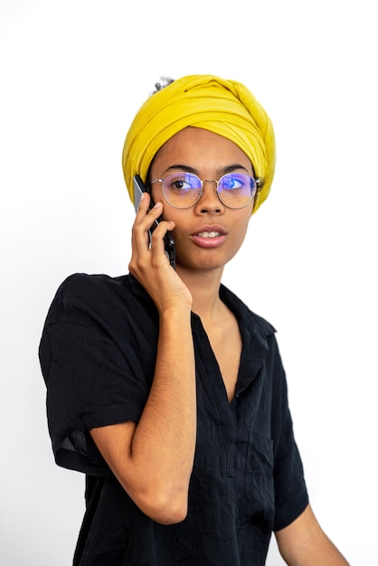 Retrato de mujer joven con gafas y pañuelo amarillo hablando por móvil sobre blanco