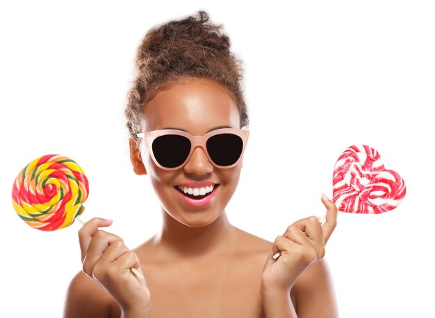 Retrato de mujer joven en gafas de sol con piruletas de colores sobre fondo blanco.