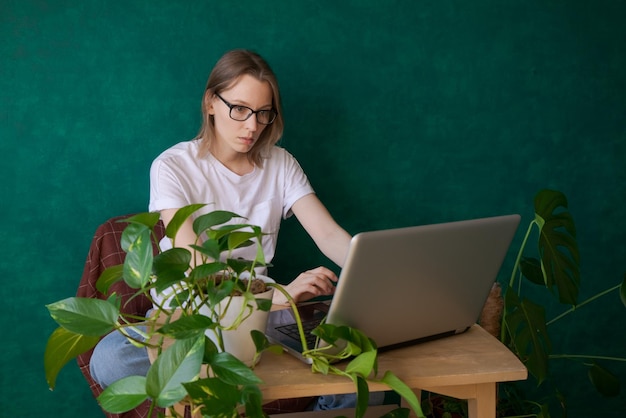 Retrato de mujer joven con gafas usando su computadora portátil mientras está sentada en el dormitorio