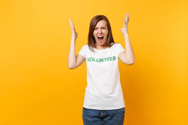 Retrato mujer joven gritando conmocionada enojada en camiseta blanca con voluntario de título verde inscripción escrito aislado sobre fondo amarillo. Ayuda de asistencia gratuita voluntaria, concepto de trabajo de gracia de caridad.