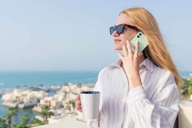 Retrato de una mujer joven hablando por teléfono y bebiendo café por la mañana