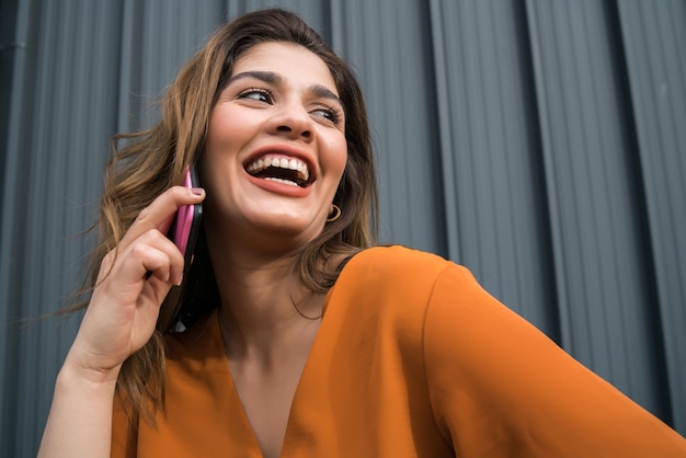 Retrato de mujer joven hablando por teléfono mientras está de pie al aire libre en la calle