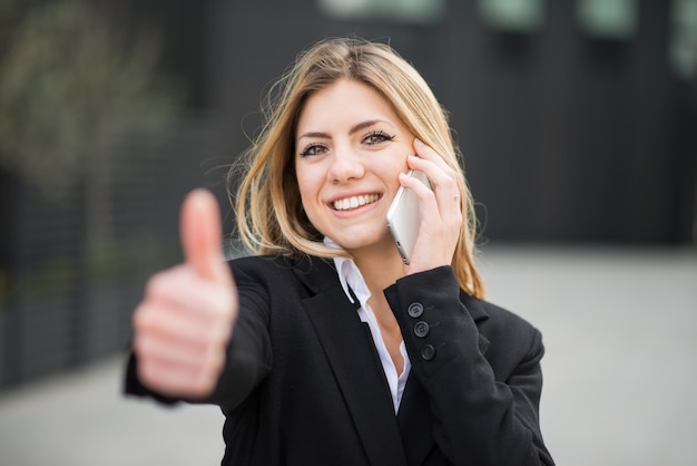 Retrato de una mujer joven hablando por teléfono y mostrando los pulgares hacia arriba al final