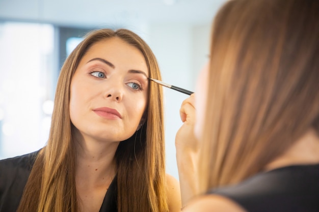 Retrato de mujer joven haciendo maquillaje cerca de espejo